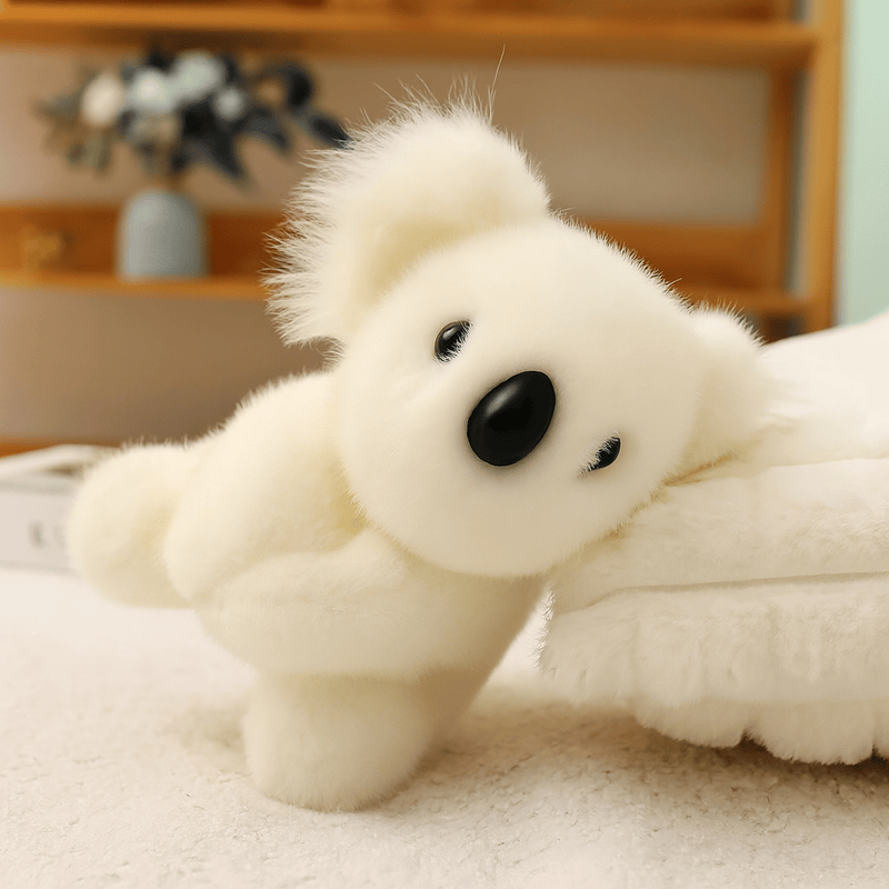 Peluche koala blanc grande famille sur une nappe sur une table adossé sur un coussin 