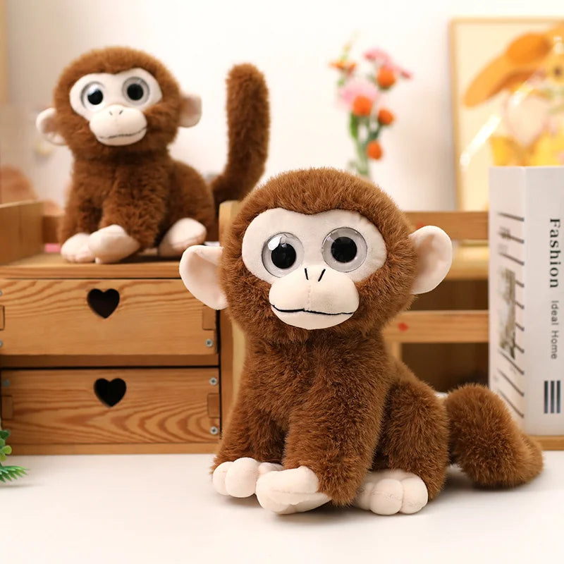 Deux peluches singes aux gros yeux, un assis sur un tiroir de meuble et l'autre assis sur une table 