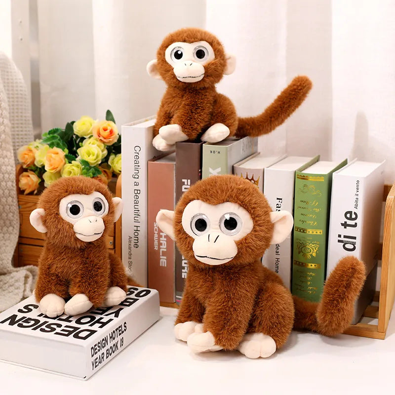Trois peluches singes aux gros yeux dont deux assis sur un livre et l'autre assis sur une table 