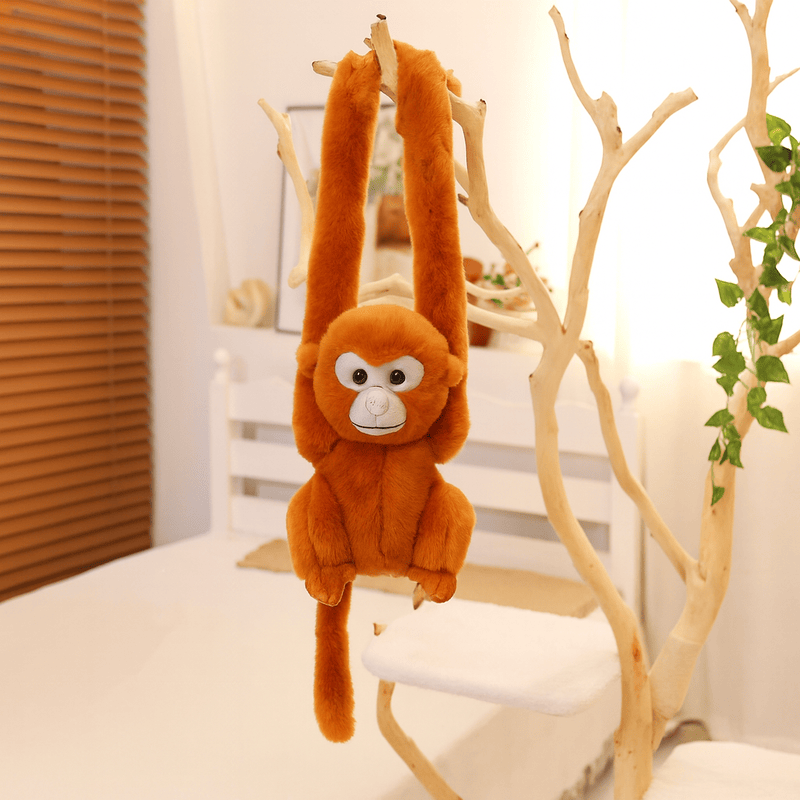 Peluche singe aux poils roux avec la tête grise suspendu par les bras sur un arbre en intérieur