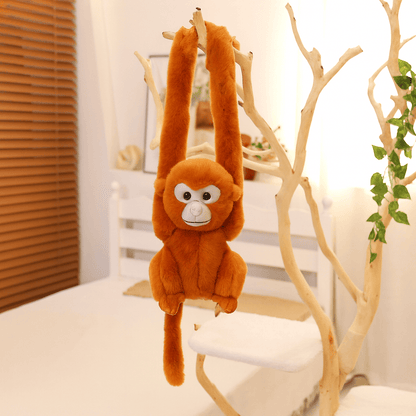 Peluche singe aux poils roux avec la tête grise suspendu par les bras sur un arbre en intérieur