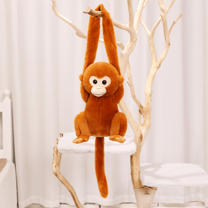 Peluche singe aux poils roux avec la tête blanche suspendu par les bras sur un arbre en intérieur
