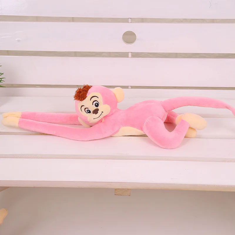 Peluche singe rose suspendu couché sur un banc